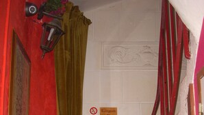 Uma escadaria com corrimãos vermelhos, uma parede vermelha, uma cortina verde e uma placa indicando a recepção no primeiro andar.