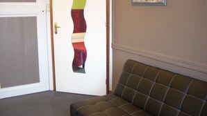 Um quarto com parede estampada, porta com design abstrato colorido e um sofá estofado marrom.