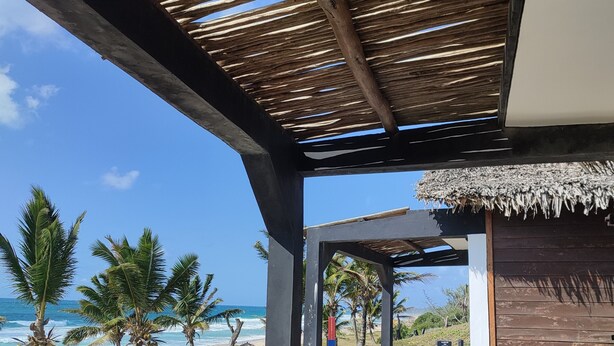 A beachside pavilion with a thatched roof, palm trees, and a view of the ocean. - Riake Resort & Villa (Nosy Boraha)