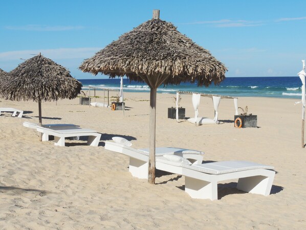 Une plage avec des chaises longues blanches et des parasols en chaume.