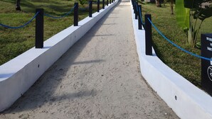 A pathway lined with palm trees and a white barrier, leading to a building with a red door. - Riake Resort & Villa (Nosy Boraha)