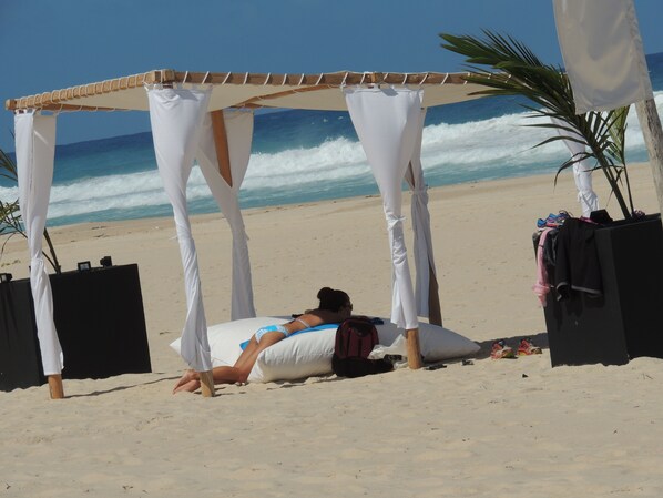 A beach scene with a canopy structure, a person lying on a beach, and a palm tree.