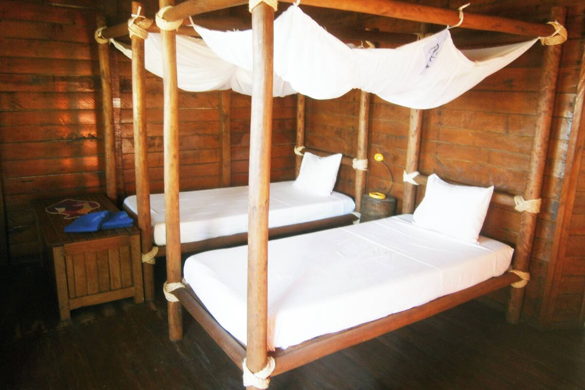 A rustic wooden cabin with two bunk beds, each with white bedding and a canopy.