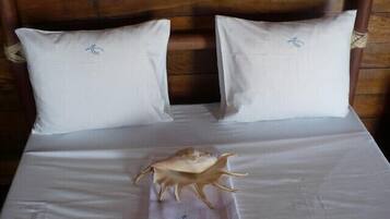 Cama con sábanas blancas y dos almohadas, cabecera de madera y una concha decorativa sobre la colcha.