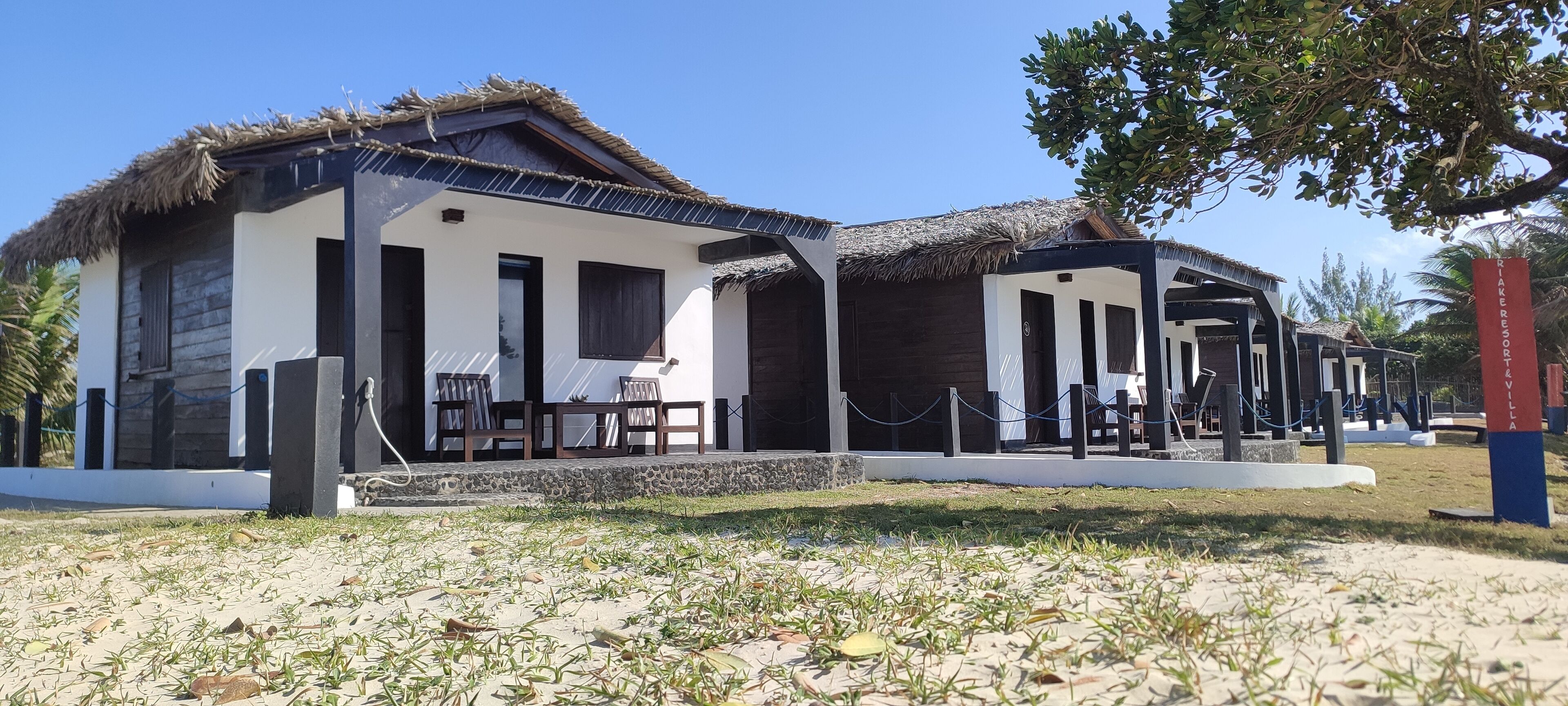 A resort with thatched-roof structures, outdoor seating, and a clear sky.