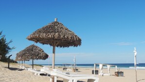 A beach with white lounge chairs and thatched umbrellas. - Riake Resort & Villa (Nosy Boraha)