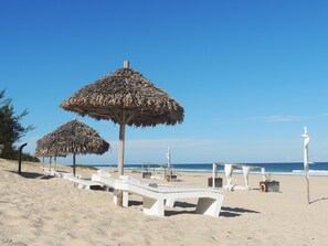 A beach with white lounge chairs and thatched umbrellas. - Riake Resort & Villa (Nosy Boraha)