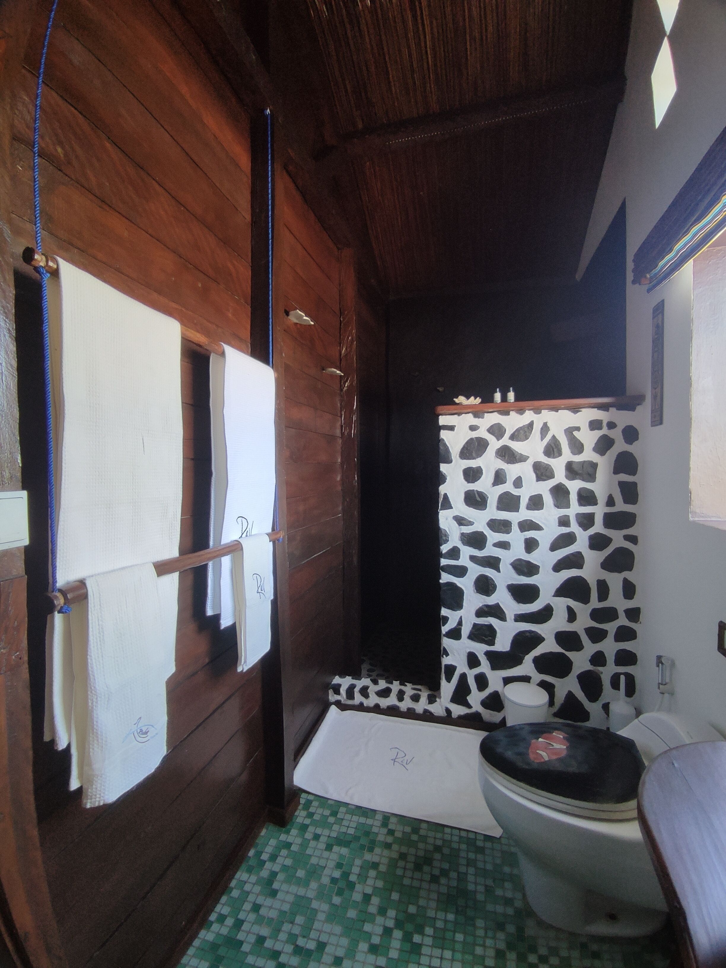 A bathroom with a wooden interior, a tiled floor, a toilet with a patterned seat cover, and a shower area with a cow print wall.