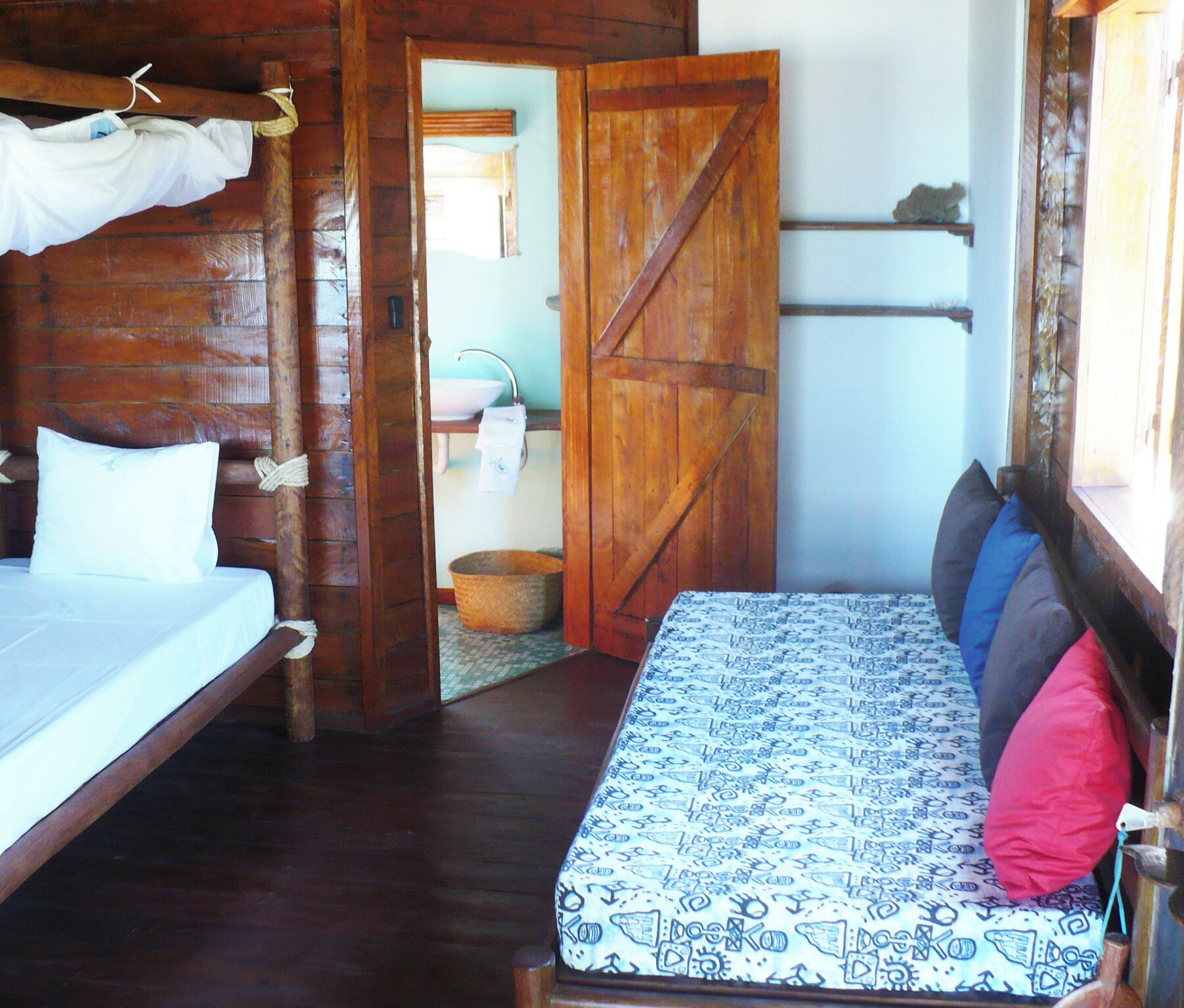 A wooden room with a bed, a wooden door, and a window.