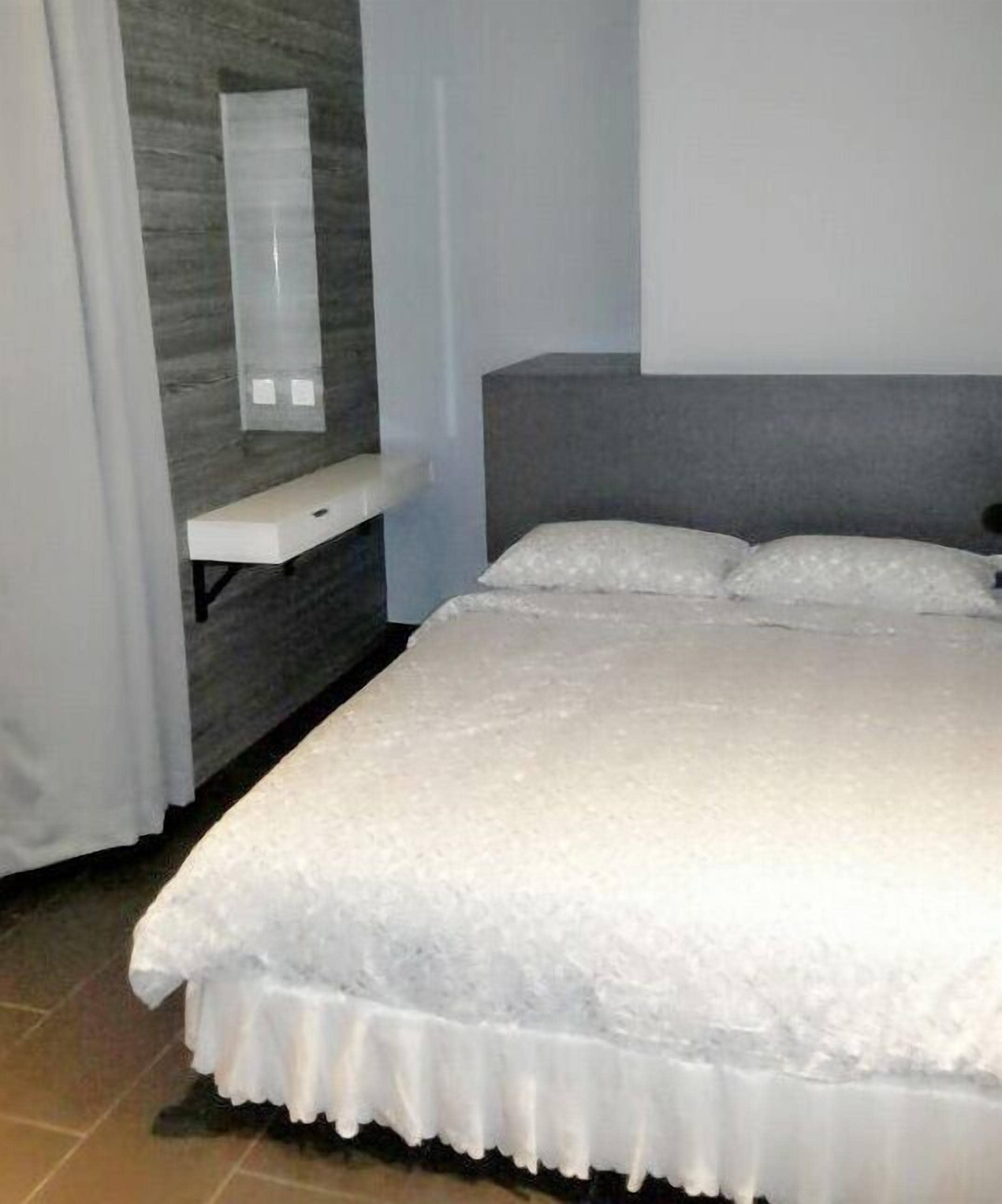 Une chambre à coucher avec un lit, une table de chevet, un miroir et une tête de lit grise.