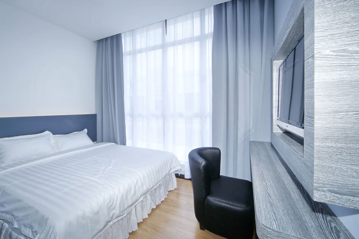 Habitación de hotel con cama, una silla y un ventanal con cortinas.