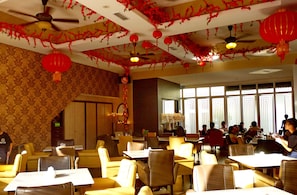 A restaurant with yellow chairs and tables, red lanterns, and a ceiling fan.