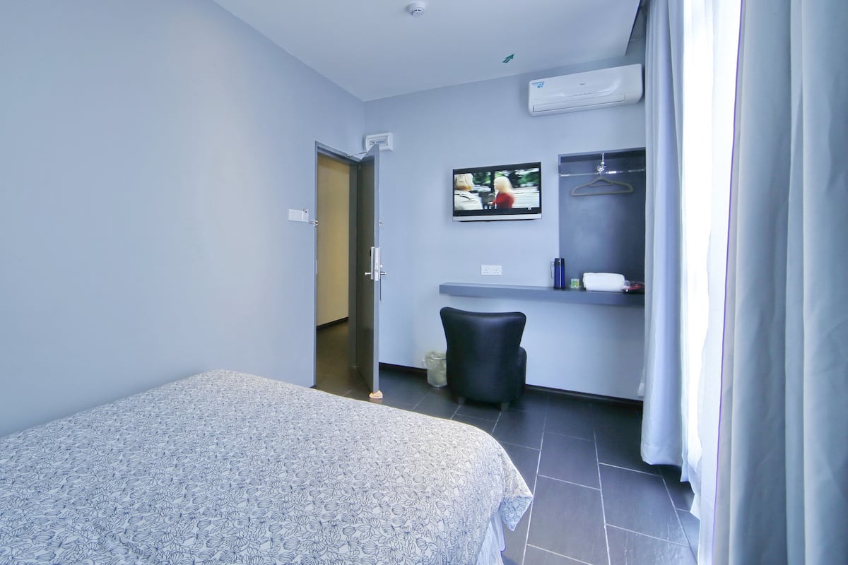 Una habitación de hotel con cama, una silla, televisor, espejo y puerta de baño.