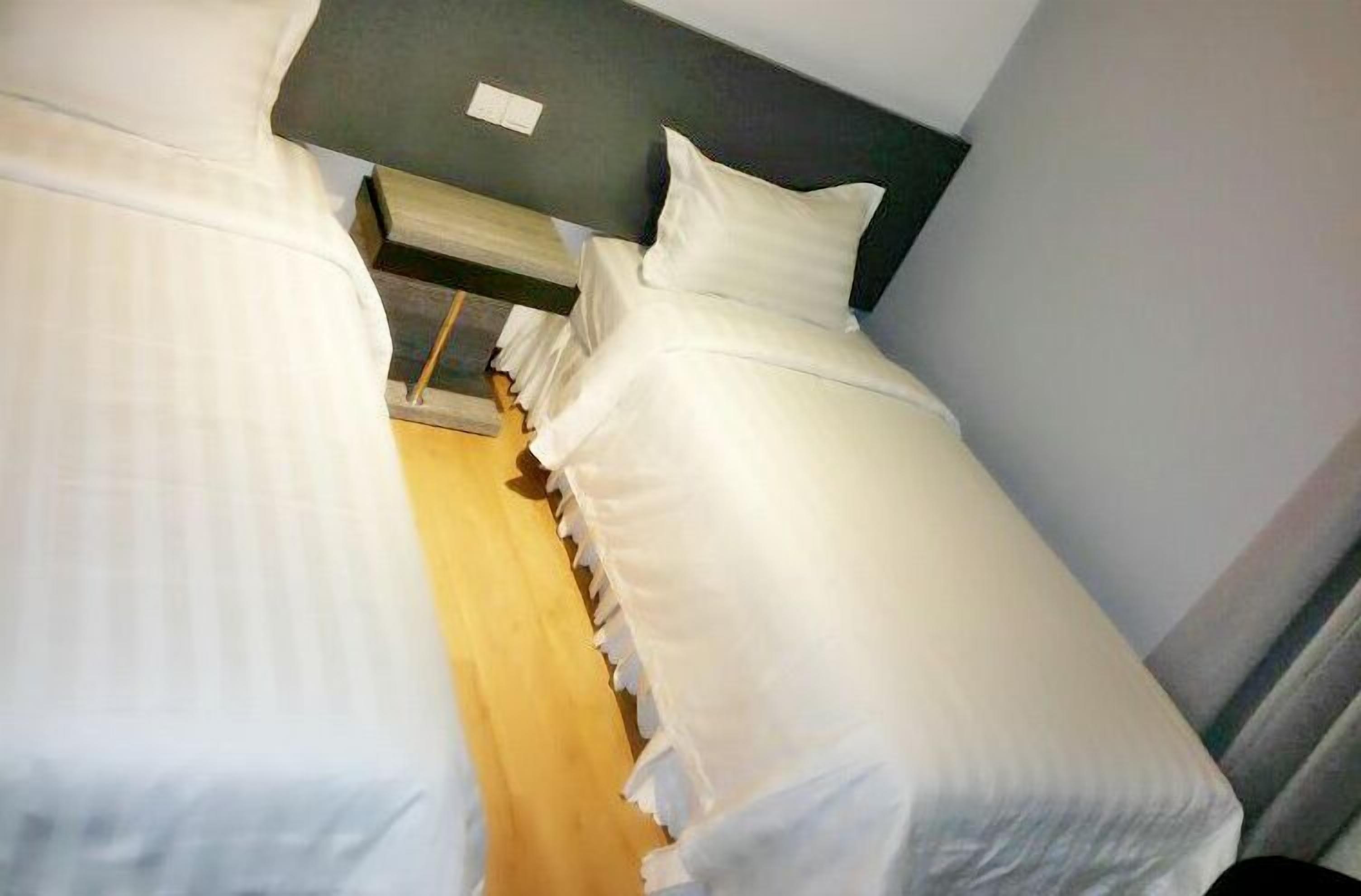 A narrow hotel room with two single beds, a wooden floor, and a dark headboard.