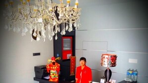 A reception area with a receptionist, a chandelier, a red wall, a counter, and a water dispenser. - My Dream Hotel (Sandakan)