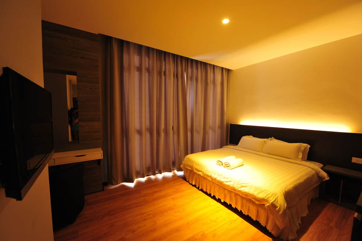 Habitación de hotel con una cama grande, un televisor de pantalla plana, piso de madera y una ventana cubierta con cortinas.