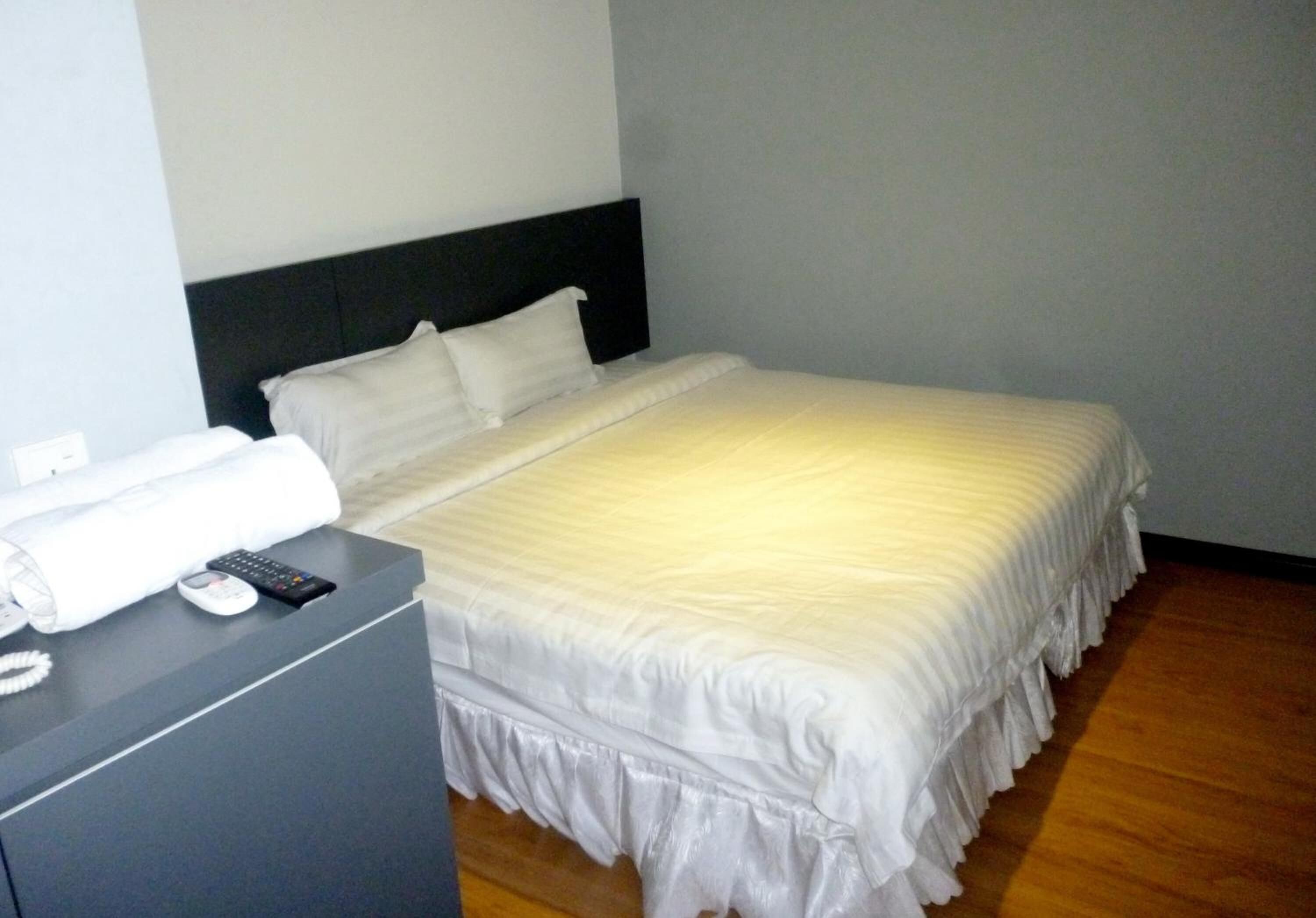 Un lit bien fait, avec une literie blanche, une tête de lit noire et une table de chevet sur laquelle se trouvent une télécommande et un téléphone.