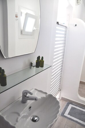 Un baño con un lavabo blanco, espejo y estantes de vidrio.