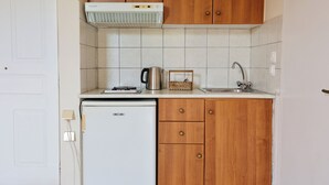 Una cocina compacta con baldosas blancas, estufa integrada, refrigerador pequeño, armarios de madera y un lavamanos.