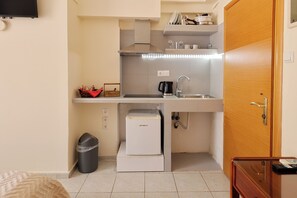 A compact kitchen with a sink, a coffee maker, a small refrigerator, and a trash bin.