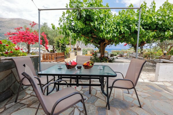An outdoor patio with a table and chairs, surrounded by stone flooring and greenery.
