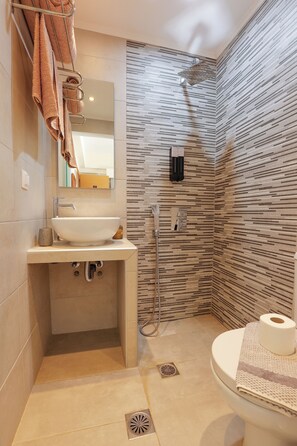 A bathroom with a sink, mirror, towel rack, shower, and toilet.