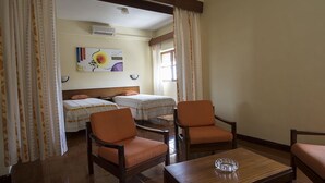 Habitación de hotel con dos camas individuales, una mesita de madera, dos sillones naranjas y un cuadro en la pared.