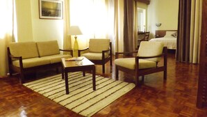 Una habitación de hotel con sofá, sillones, una mesita, una lámpara y una cama.
