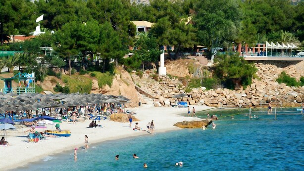 Una playa con sombrillas, gente nadando y un litoral rocoso.