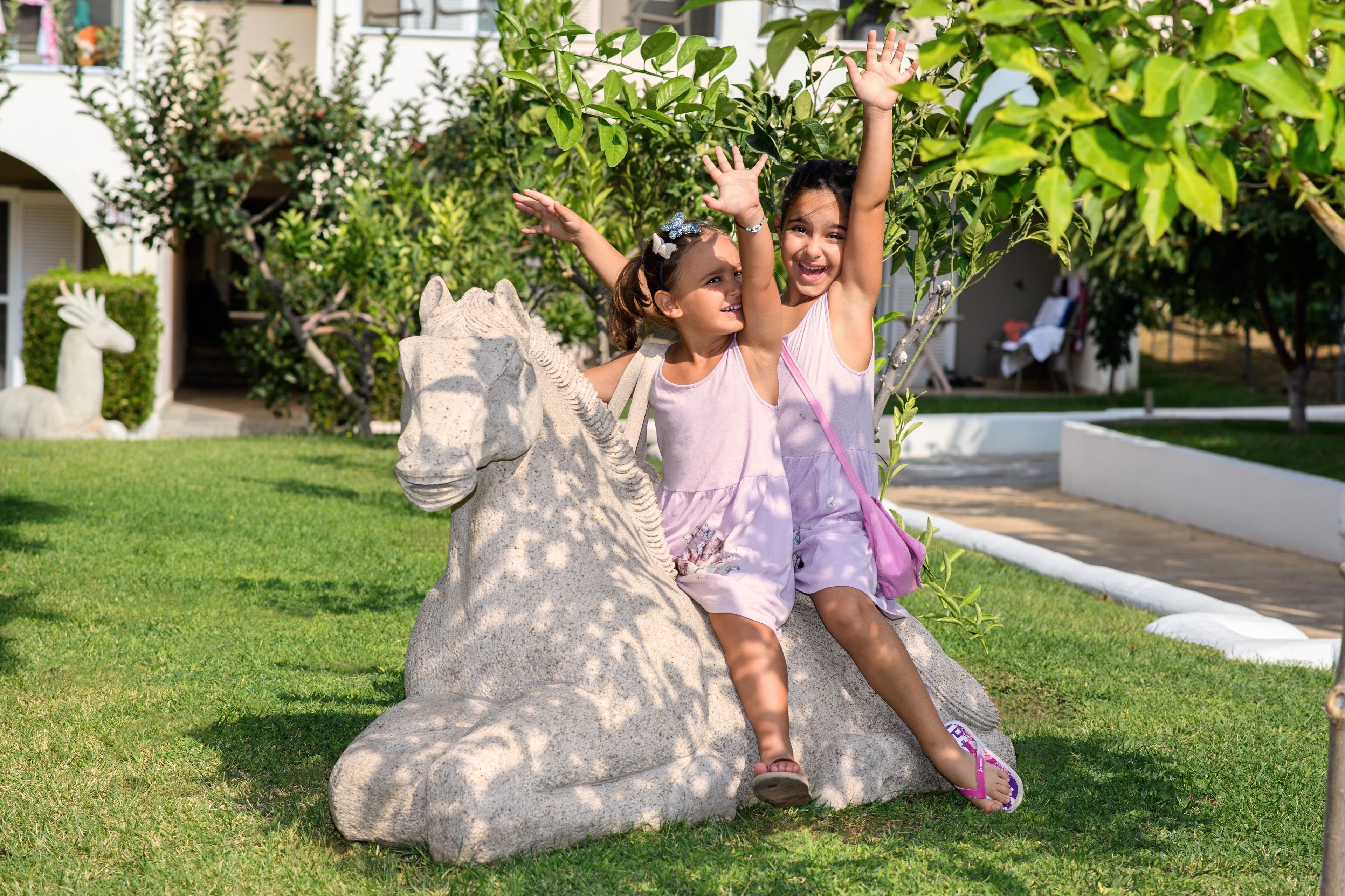 Two children playing on a grassy lawn with a stone sculpture and a building in the background.