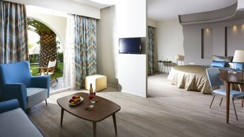 Habitación de hotel moderna con techo curvo, televisor de pantalla plana, cama con ropa de cama azul, zona de comedor con mesa y sillas, y balcón con vistas a un jardín y una palmera.