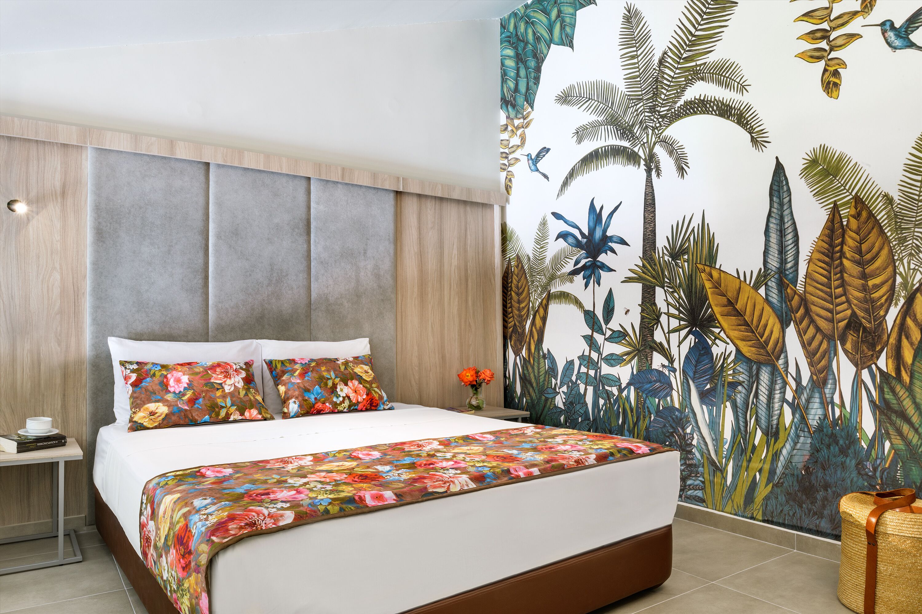 A bedroom with a large bed, a wooden headboard, a floral-patterned bedspread, and a tropical-themed wall mural.