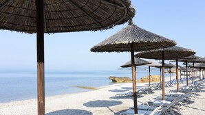 Una spiaggia con ombrelloni di paglia e lettini bianchi.