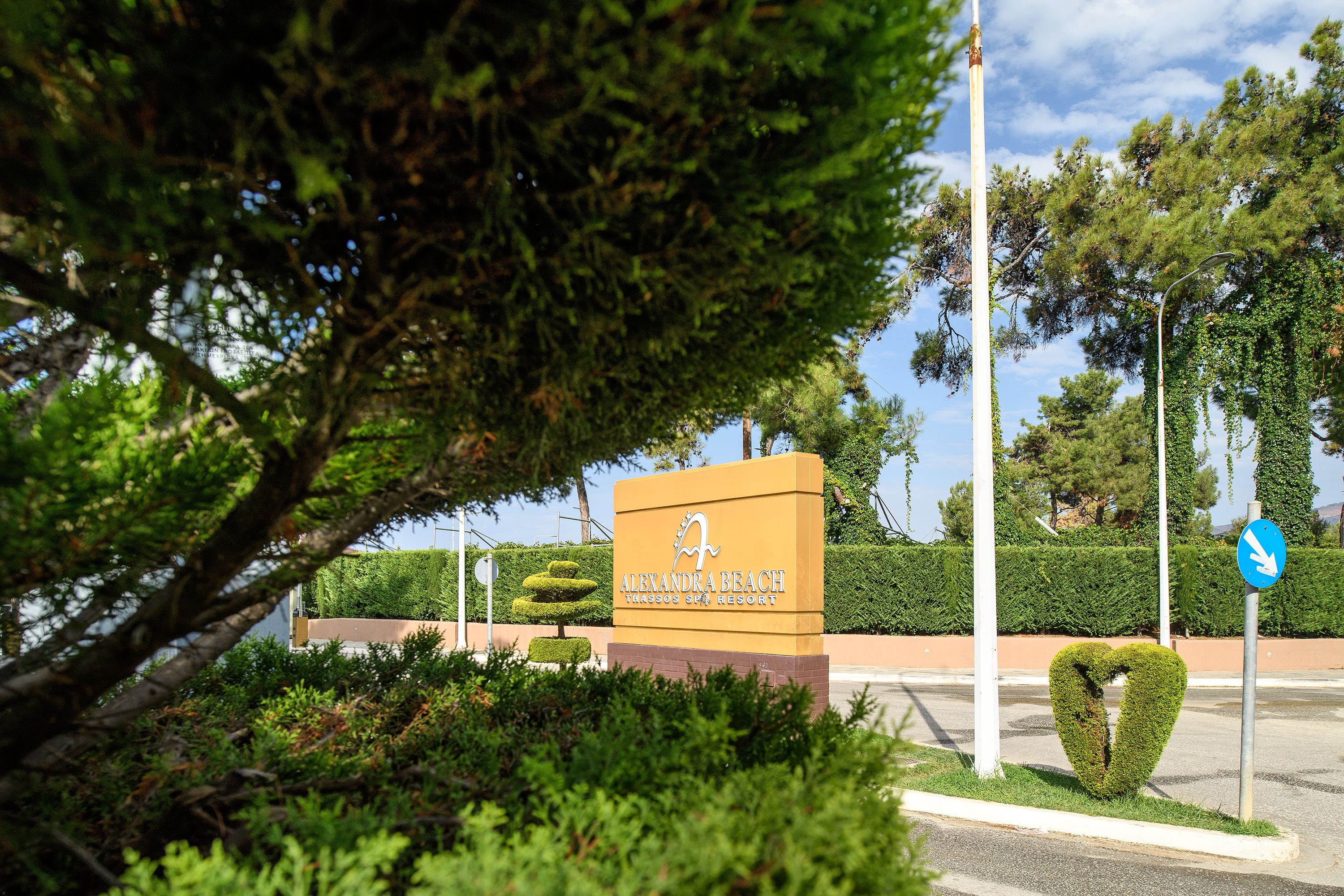 A sign for Alexandria Beach Resort with a heart-shaped bush and a directional arrow sign.