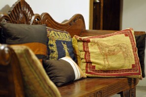 A wooden sofa with multiple cushions, including a decorative one with a horse design. - Palazzo Osanna (Nardò)