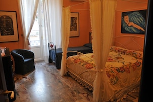 A bedroom with a four-poster bed, a chair, a desk, and a window with curtains.