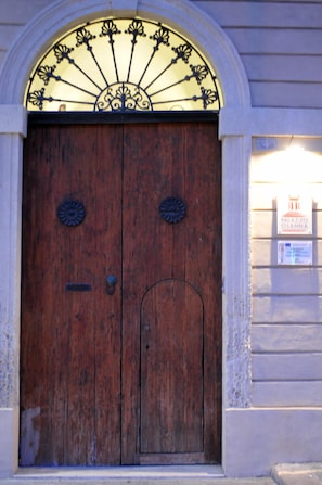 A wooden double door with a decorative metal arch above it. - Palazzo Osanna (Nardò)