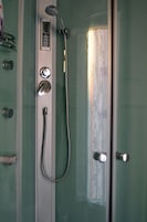 A shower with a digital control panel, a handheld showerhead, and a glass door.