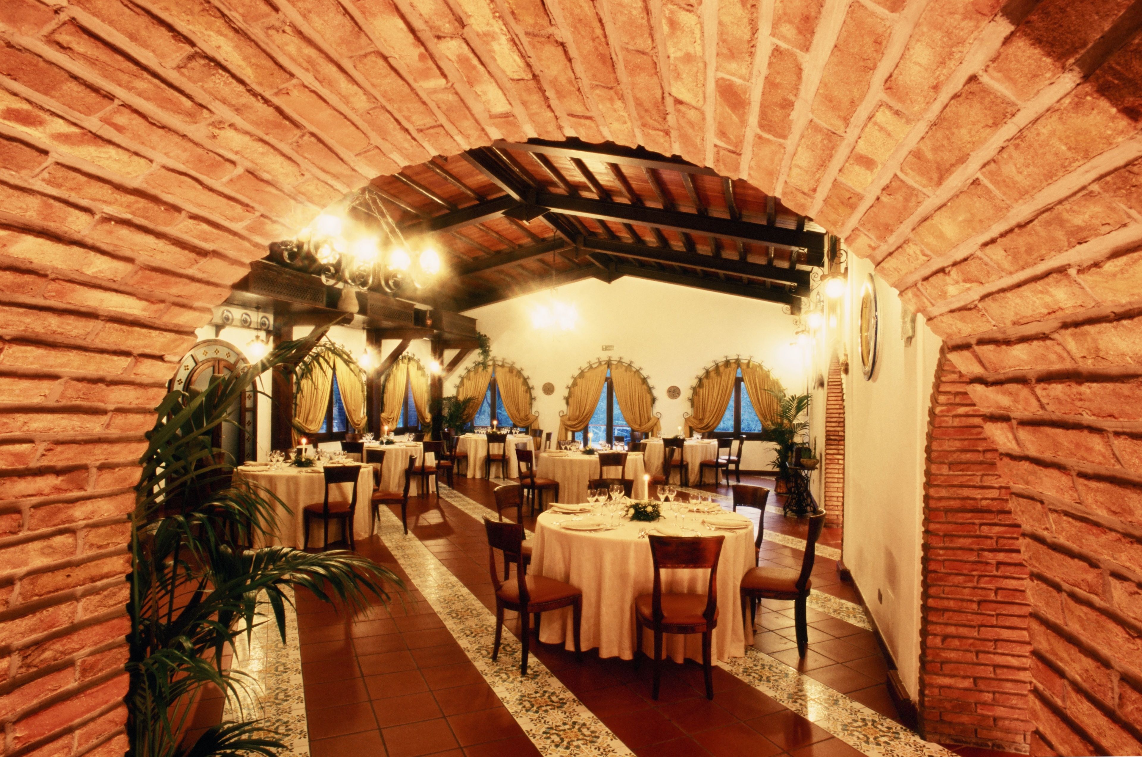 A restaurant with brick walls, round tables, and chandeliers.