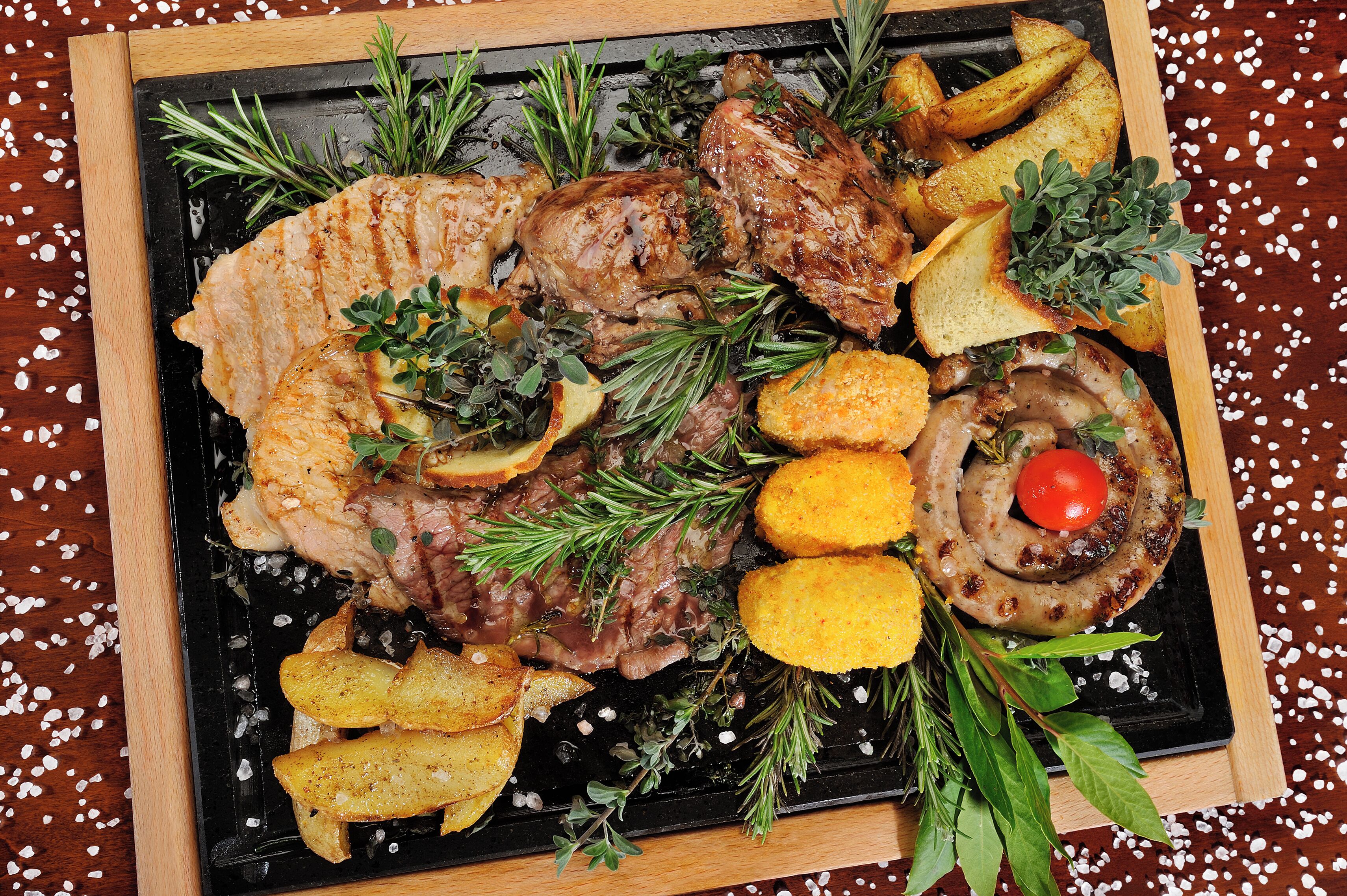 A roasted pork loin with potatoes and rosemary on a black slate plate.