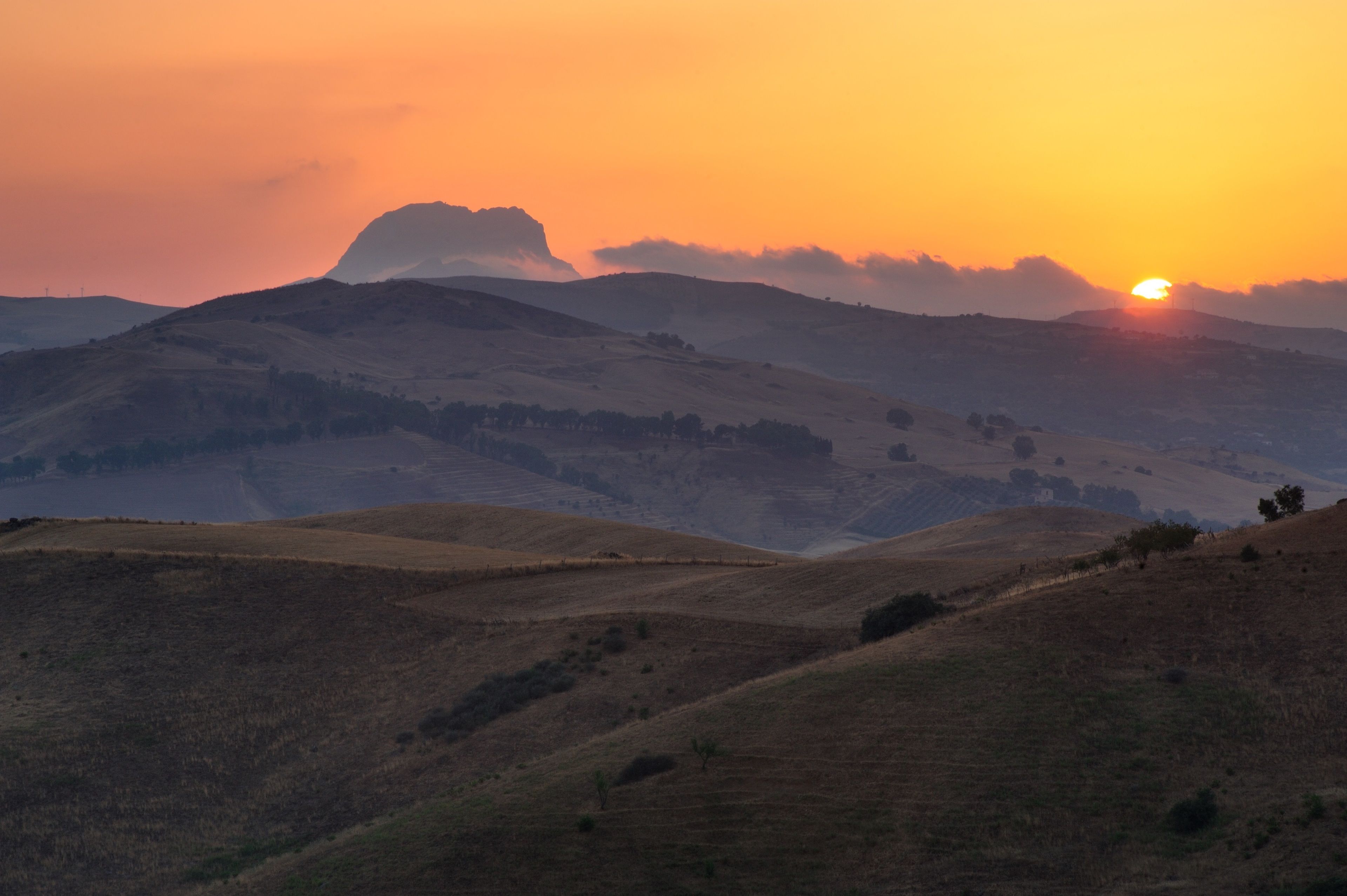 A landscape with rolling hills and a sunset.
