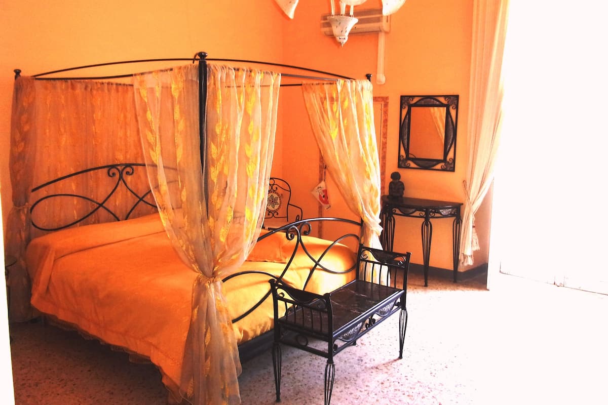A four-poster bed with a canopy, a small bedside table, and a mirror on the wall.