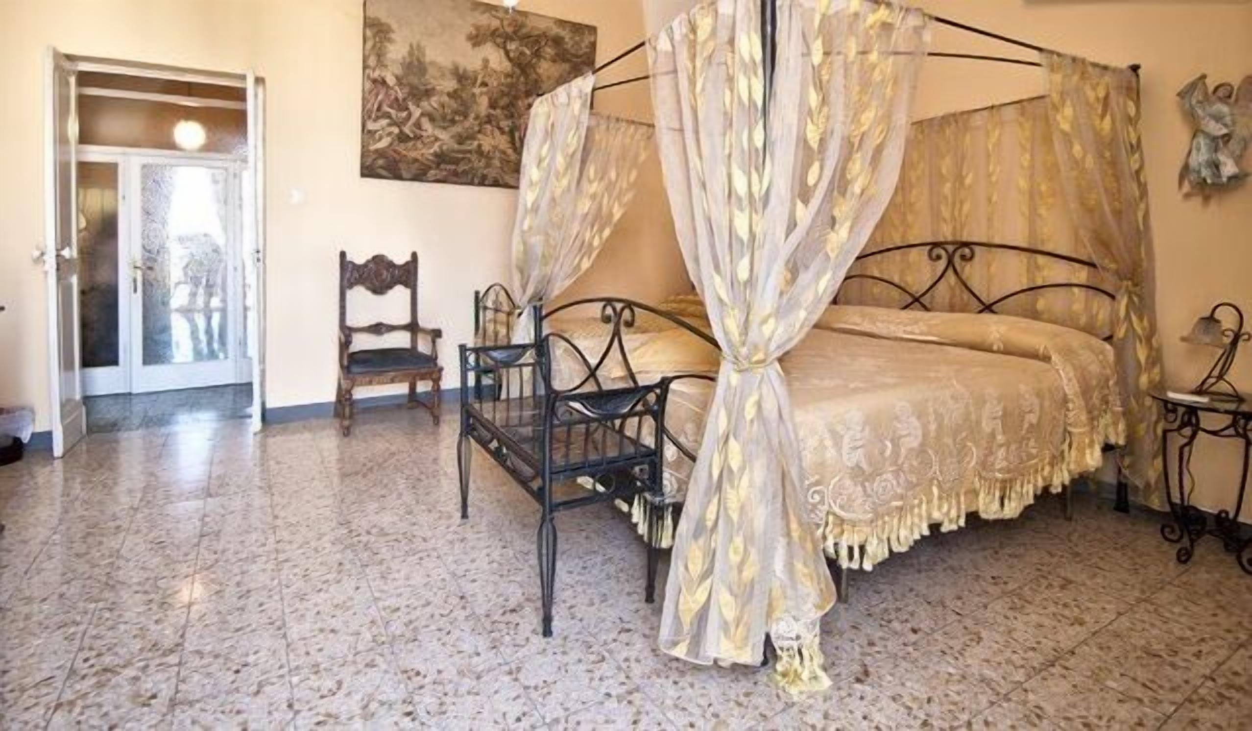 A bedroom with a four-poster bed, a chair, and a small table.