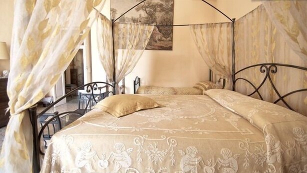 A four-poster bed with a canopy, a painting on the wall, and a view of the outdoors. - Angeli dell'Osanna B&B (Nardò)
