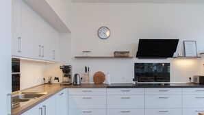 A modern kitchen with white cabinetry, a stainless steel sink, a flat-screen TV, and a clock on the wall.