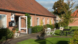 A brick building with a red-tiled roof, a garden area with a table and chairs, and a bicycle with a sign.