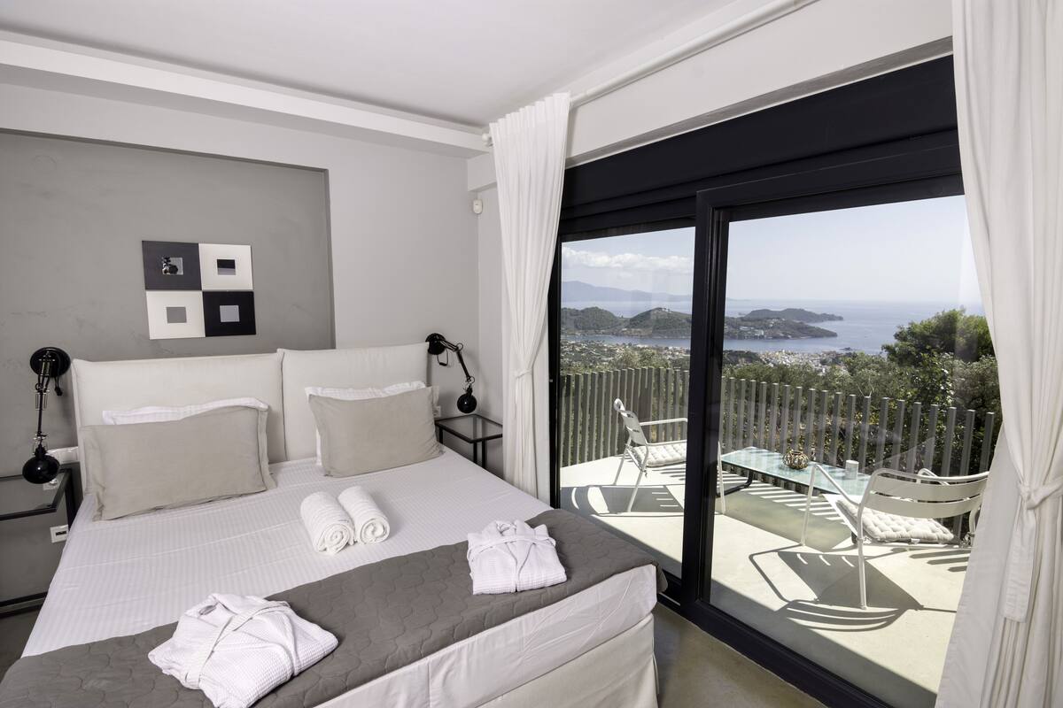 A modern hotel room with a large bed, a view of the sea, and a balcony with outdoor furniture.