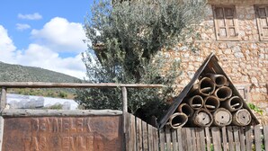 Une clôture en bois rustique, sur laquelle est accrochée une pancarte indiquant « Beymelek Tas Evler », et une pile de bûches.