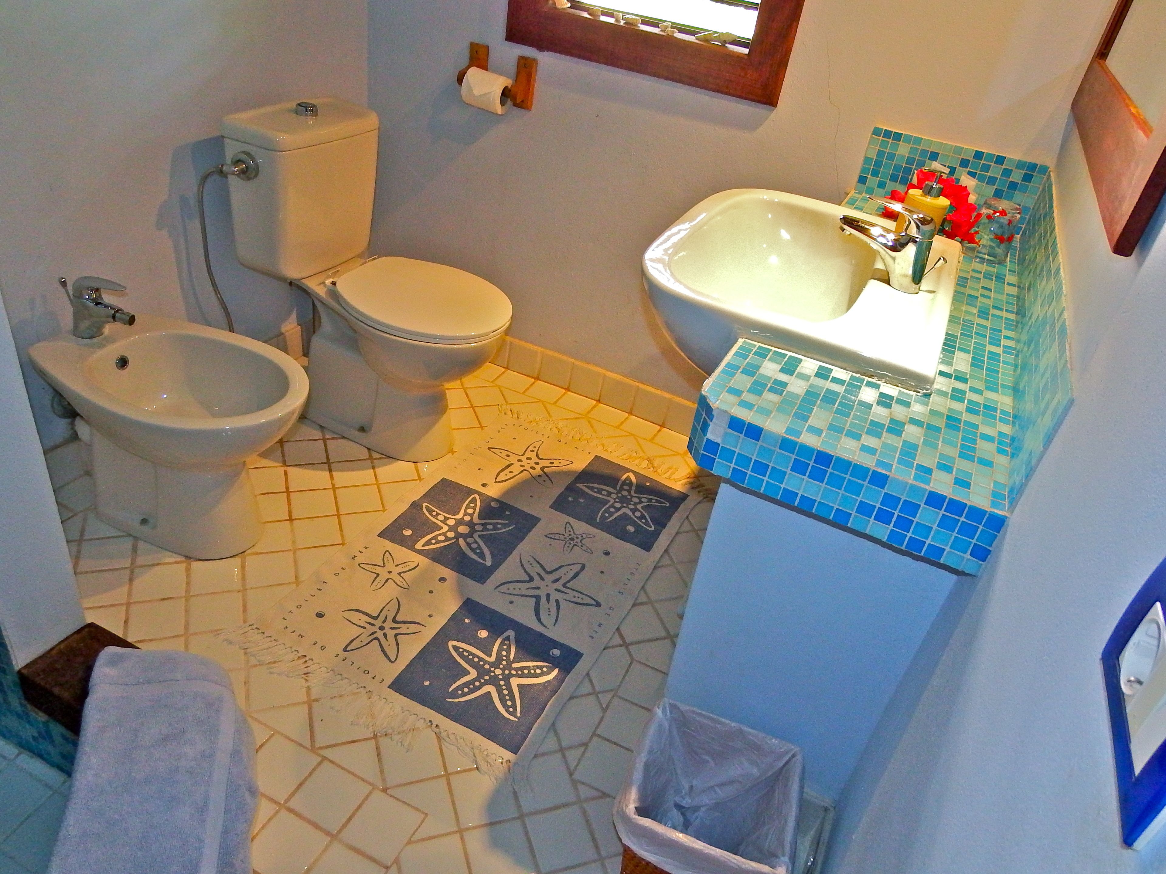 Une salle de bain comprenant des toilettes, un bidet, un lavabo et un carrelage décoré de motifs d’étoiles de mer.