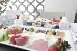 A variety of cheeses, meats, and fruits on a white platter.